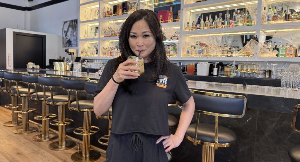 A woman sips a drink from a straw in a restaurant, with a bar behind her