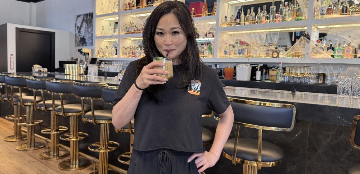 A woman sips a drink from a straw in a restaurant, with a bar behind her