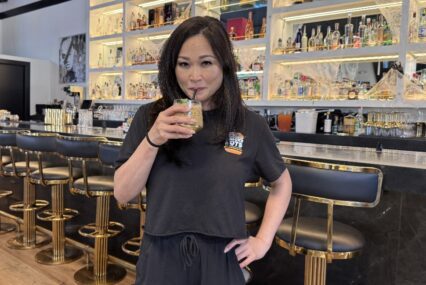 A woman sips a drink from a straw in a restaurant, with a bar behind her