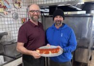 Two men holding a stromboli in the kitchen of a restaurant in San Jose, California