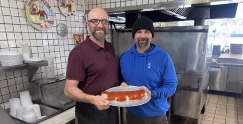 Two men holding a stromboli in the kitchen of a restaurant in San Jose, California