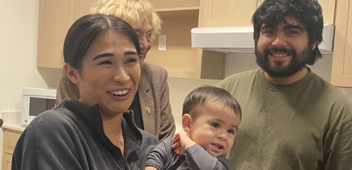 Trợ cấp chăm sóc liên tục--Kaytanna Alvarido và Alberto Barragan San Jose Một người phụ nữ đang bế một đứa trẻ nhỏ đứng cạnh một người đàn ông trong bếp