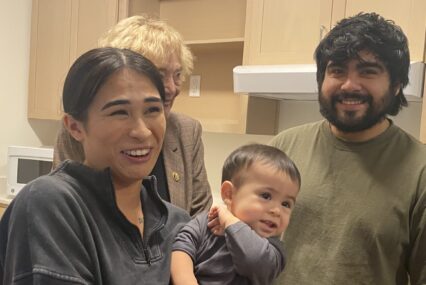 A woman holding a young child stands next to a man in a kitchen