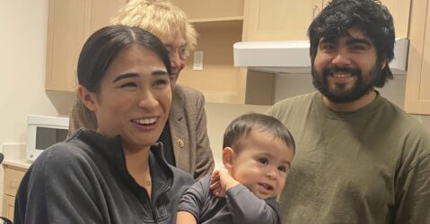 A woman holding a young child stands next to a man in a kitchen