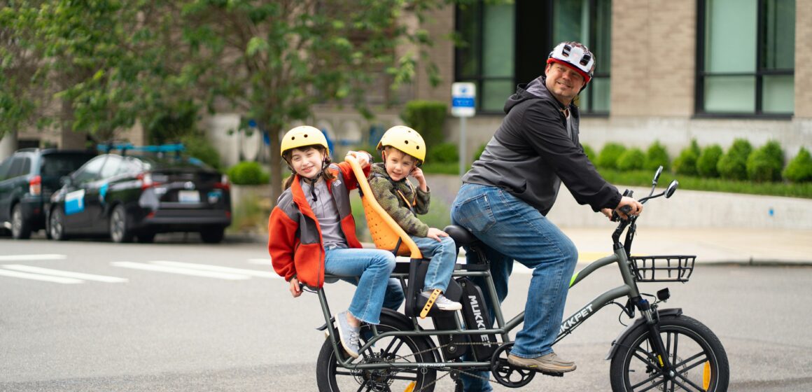 Một người cha và hai đứa con đi xe đạp điện