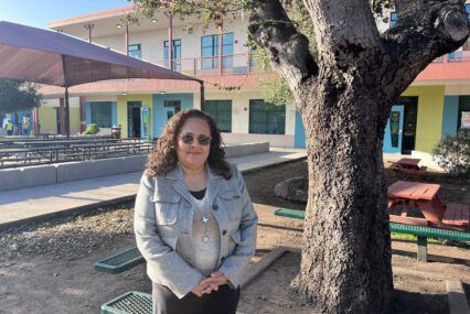 A woman stands next to a tree outside a school in East San Jose, California