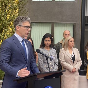 HUD Lawsuit Tony LoPresti San Jose A man in a suit and tie speaks into a microphone at a podium, with people standing behind him