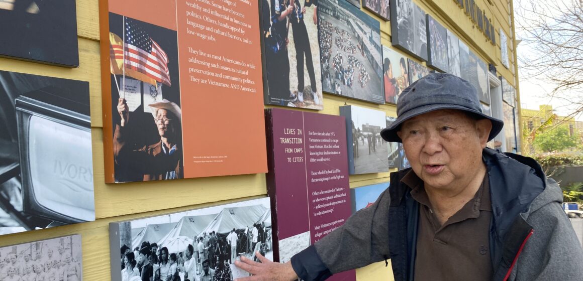 An older Vietnamese man in a bucket hat and coat stands next to a museum exhibit in San Jose, California
