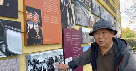 An older Vietnamese man in a bucket hat and coat stands next to a museum exhibit in San Jose, California