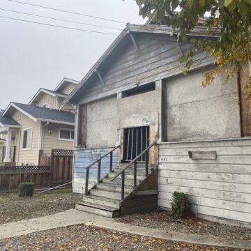 681 N 5th St. A boarded up wooden building next to a tan home.