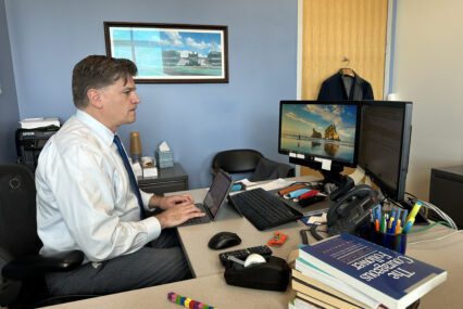 A man types on a keyboard at a desk in an office