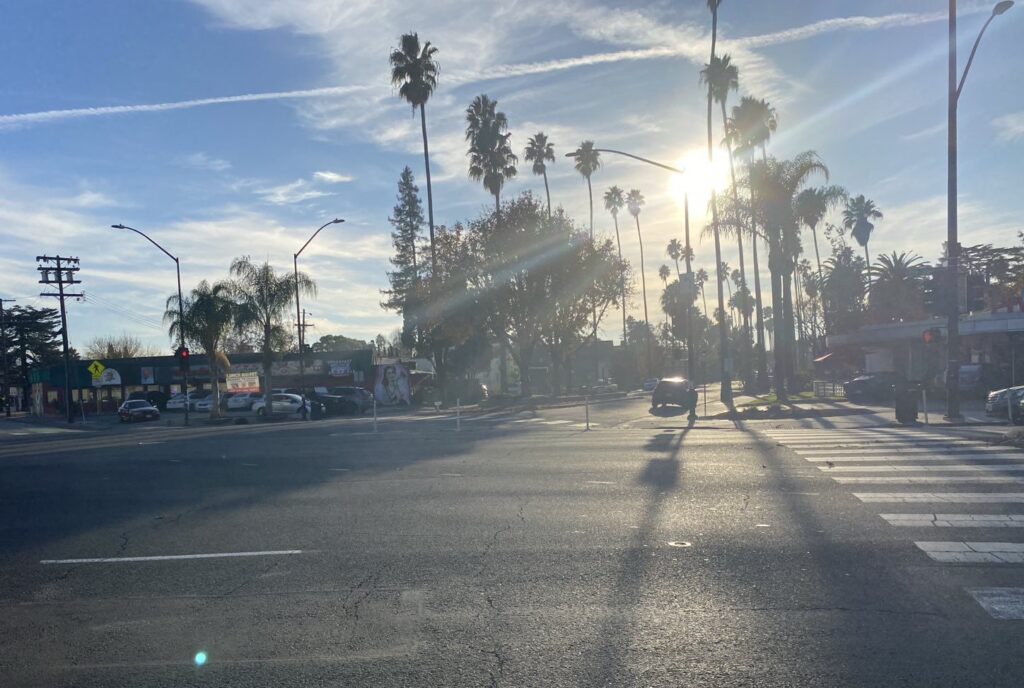 A bright evening sun hangs low over a street intersection.