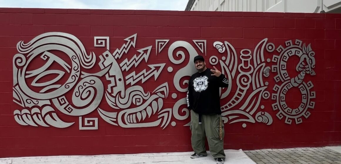 An artist stands with a metal mural on the side of a fire station in San Jose, California