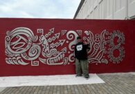An artist stands with a metal mural on the side of a fire station in San Jose, California