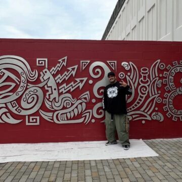 An artist stands with a metal mural on the side of a fire station in San Jose, California