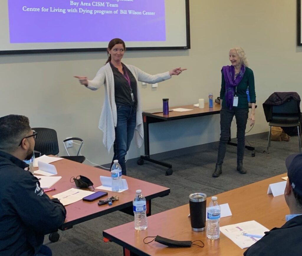 Two women present in a classroom in front of people sitting at desks.