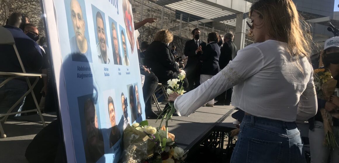 A woman presents flowers to a memorial poster board at a vigil.