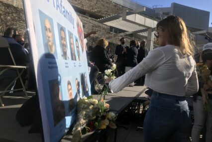 A woman presents flowers to a memorial poster board at a vigil.