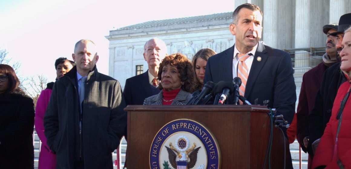 A man stands at a podium outside with other people behind him