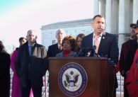A man stands at a podium outside with other people behind him