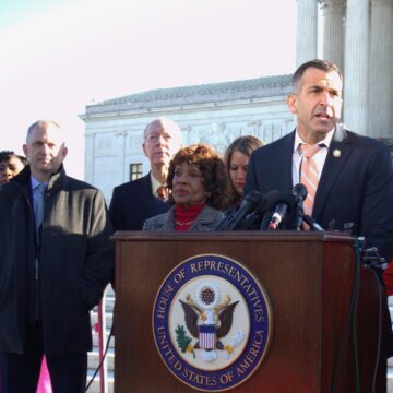 LICCARDO A man stands at a podium outside with other people behind him