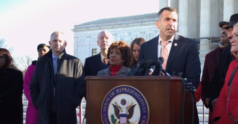 A man stands at a podium outside with other people behind him