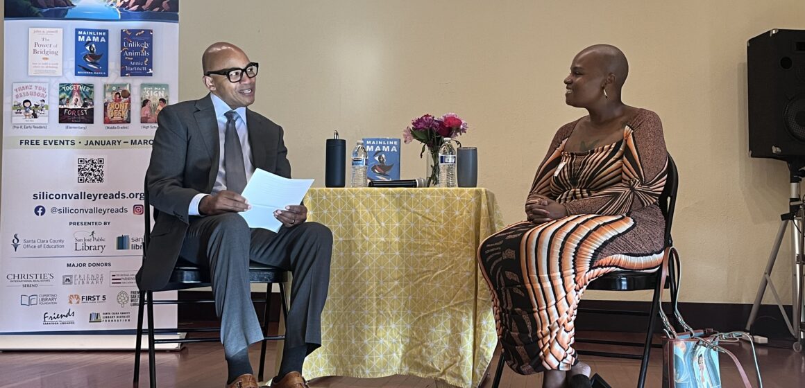 A man and a woman sitting in chairs with a table between them onstage in San Jose, California
