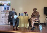 A man and a woman sitting in chairs with a table between them onstage in San Jose, California