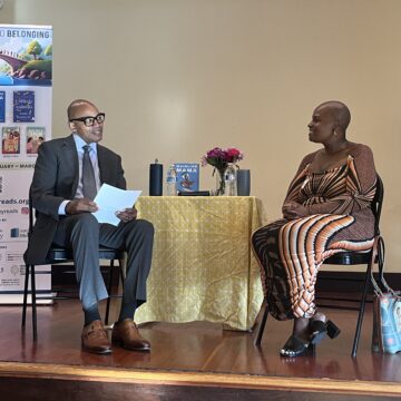 A man and a woman sitting in chairs with a table between them onstage in San Jose, California