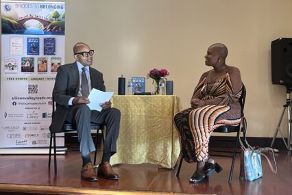 A man and a woman sitting in chairs with a table between them onstage in San Jose, California