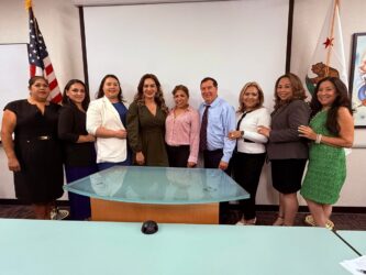 Hispanic Chamber Swearing In A row of people pose in front of a wall with flags in an office.