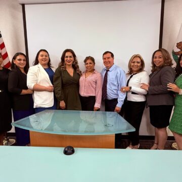A row of people pose in front of a wall with flags in an office.