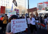 Photo of a group of people marching in front of the San Jose Convention Center, holding signs reading "INHUMANE CRUEL EVIL Due Process is American" and "LATINAS CONTRA ICE!!"