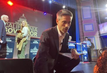 A man bending down on stage to speak to the audience in San Francisco, California