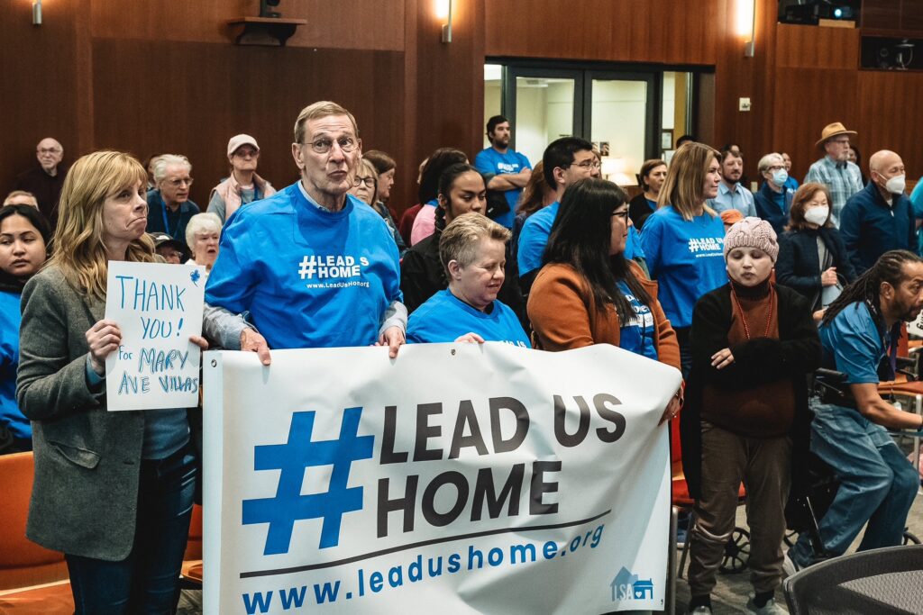 People stand holding signs at a government meeting in Cupertino, California