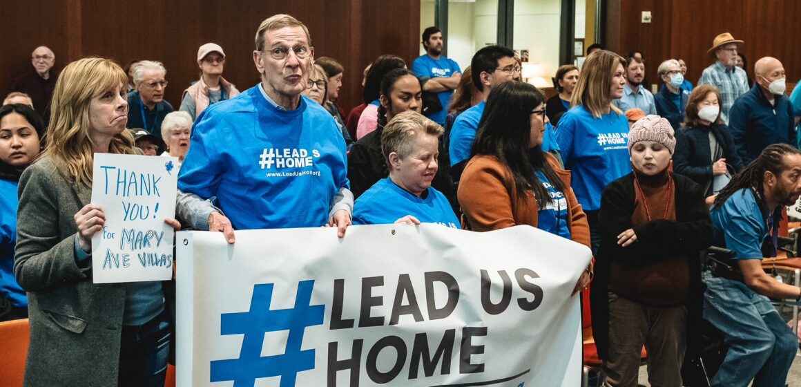 People stand holding signs at a government meeting in Cupertino, California