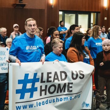 People stand holding signs at a government meeting in Cupertino, California