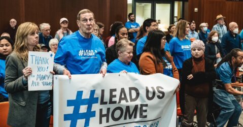 People stand holding signs at a government meeting in Cupertino, California