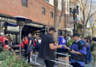 A man shows his ID to a bouncer to get into a bar. In the background, a large crowd is gathered.