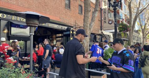 A man shows his ID to a bouncer to get into a bar. In the background, a large crowd is gathered.