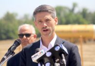 A man in a suit jacket speaks into microphones at a podium during an outdoor news conference in San Jose, California