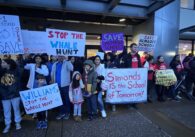 Un grupo de personas sostiene carteles afuera de una oficina del distrito escolar en San José, California.