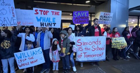 Un grupo de personas sostiene carteles afuera de una oficina del distrito escolar en San José, California.