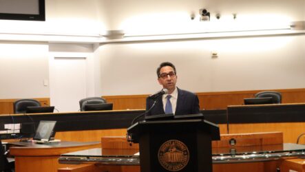 DA Rosen A man in a suit speaks at a podium at a government meeting in Santa Clara County, California