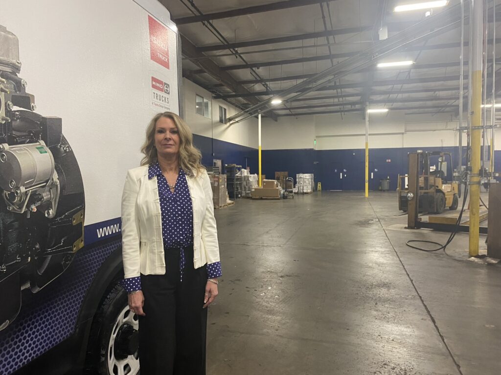 A woman in a white blazer stands in a warehouse.