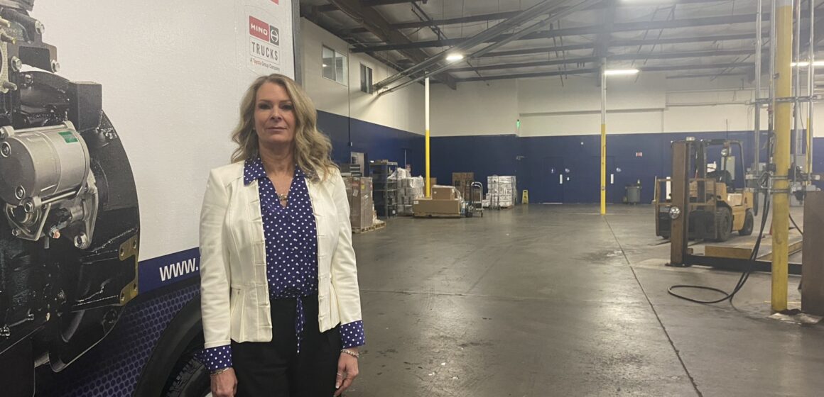 A woman in a white blazer stands in a warehouse.