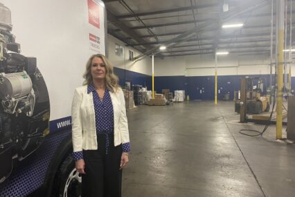 A woman in a white blazer stands in a warehouse.