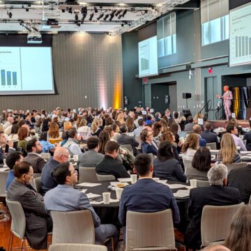 A crowd of people seated at tables watching a man speak onstage in San Jose, California