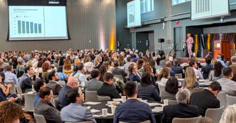 A crowd of people seated at tables watching a man speak onstage in San Jose, California