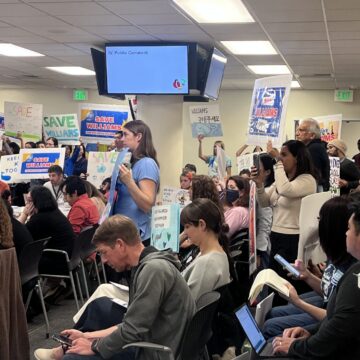 People holding up protest signs at a school board meeting in San Jose, California